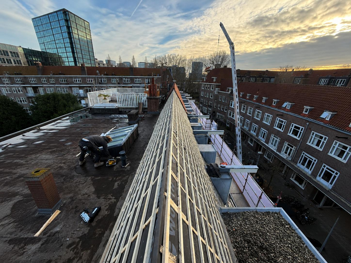 Dakrenovatie op een hellend dak: houten panlatten op waterdicht onderdak langs de nok, dakdekker aan het werk, kraan en steiger bij een stedelijk renovatieproject door Nouwen Bouw & Dakservice